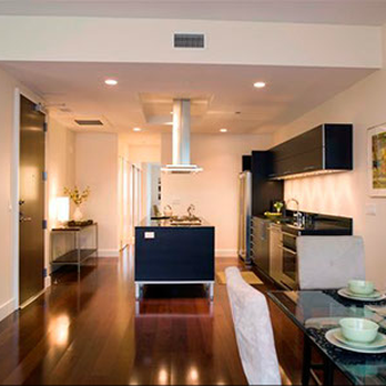 A modern kitchen with sleek black cabinetry, a central island, and dining area, designed by Tycon Builders Inc. in San Francisco.